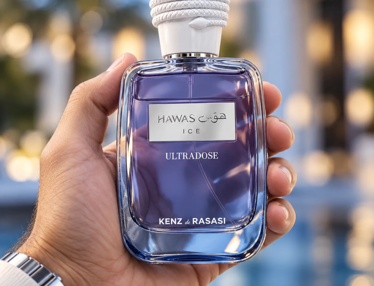 Kenz de Rasasi Hawas Ice Ultradose by Kenz de Rasasi 100ml Men — A hand holds a clear glass perfume bottle with purple liquid and a white cap, against a blurred outdoor background with lights.
