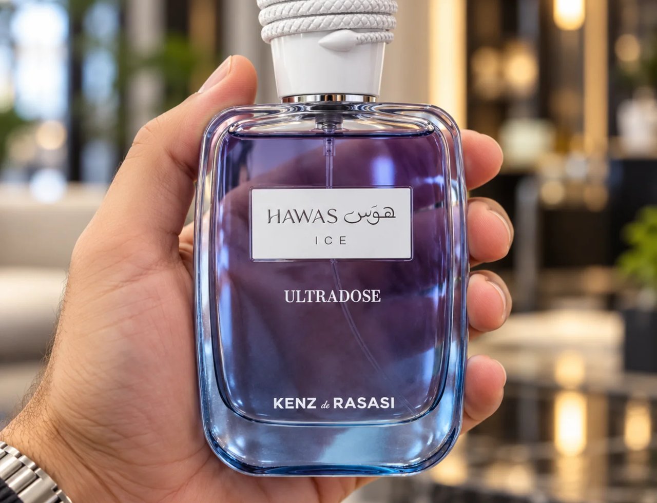 Kenz de Rasasi Hawas Ice Ultradose 100ml Lelaki — Tangan memegang botol minyak wangi kaca jernih berisi cecair ungu, bertutup tali putih dan label putih dengan tulisan Arab dan Inggeris.