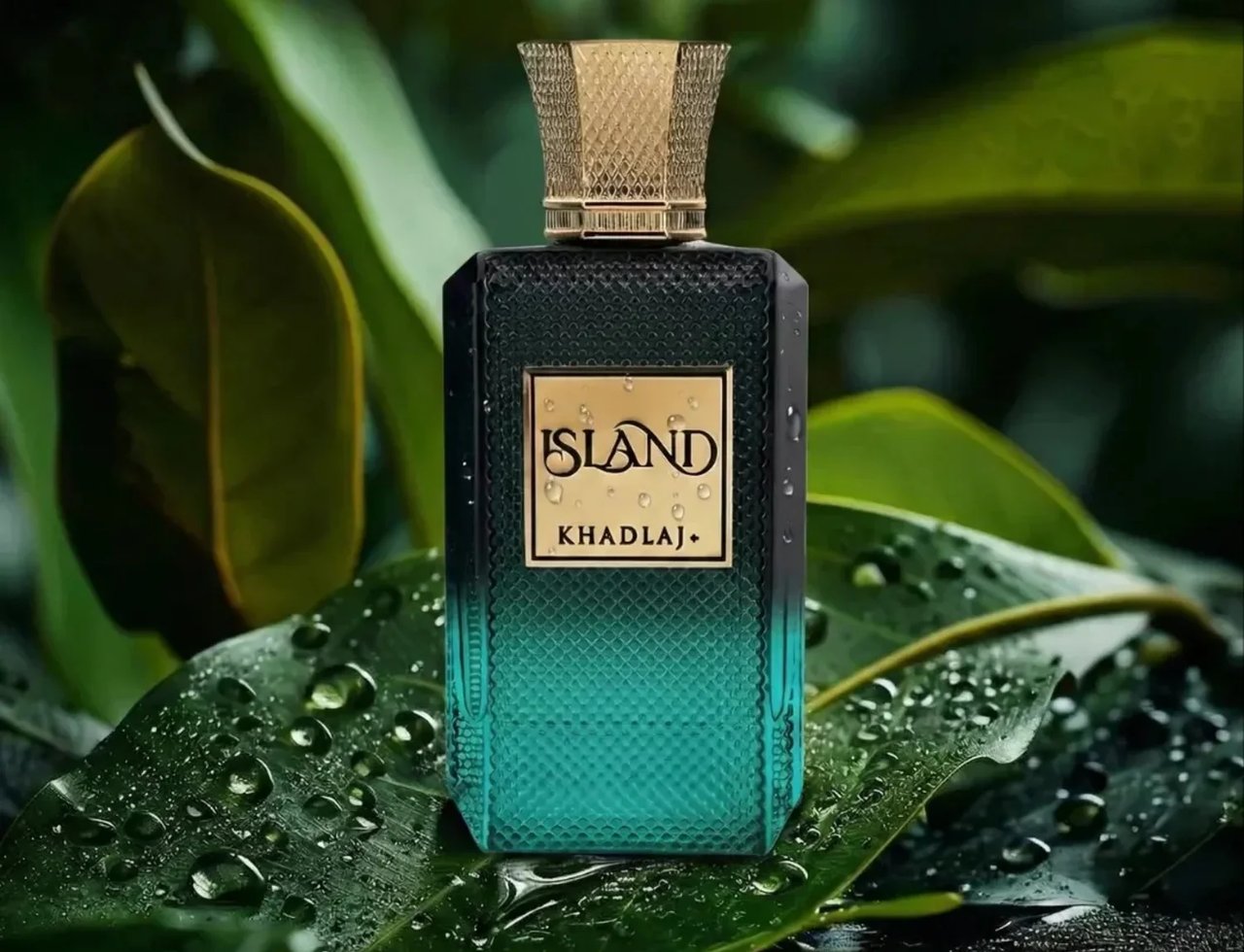 Khadlaj Island Extrait de Parfum 100ml by Khadlaj — Botol minyak wangi berwarna hijau kebiruan gelap dengan penutup emas bertekstur, diletakkan di atas daun hijau basah dengan titisan air