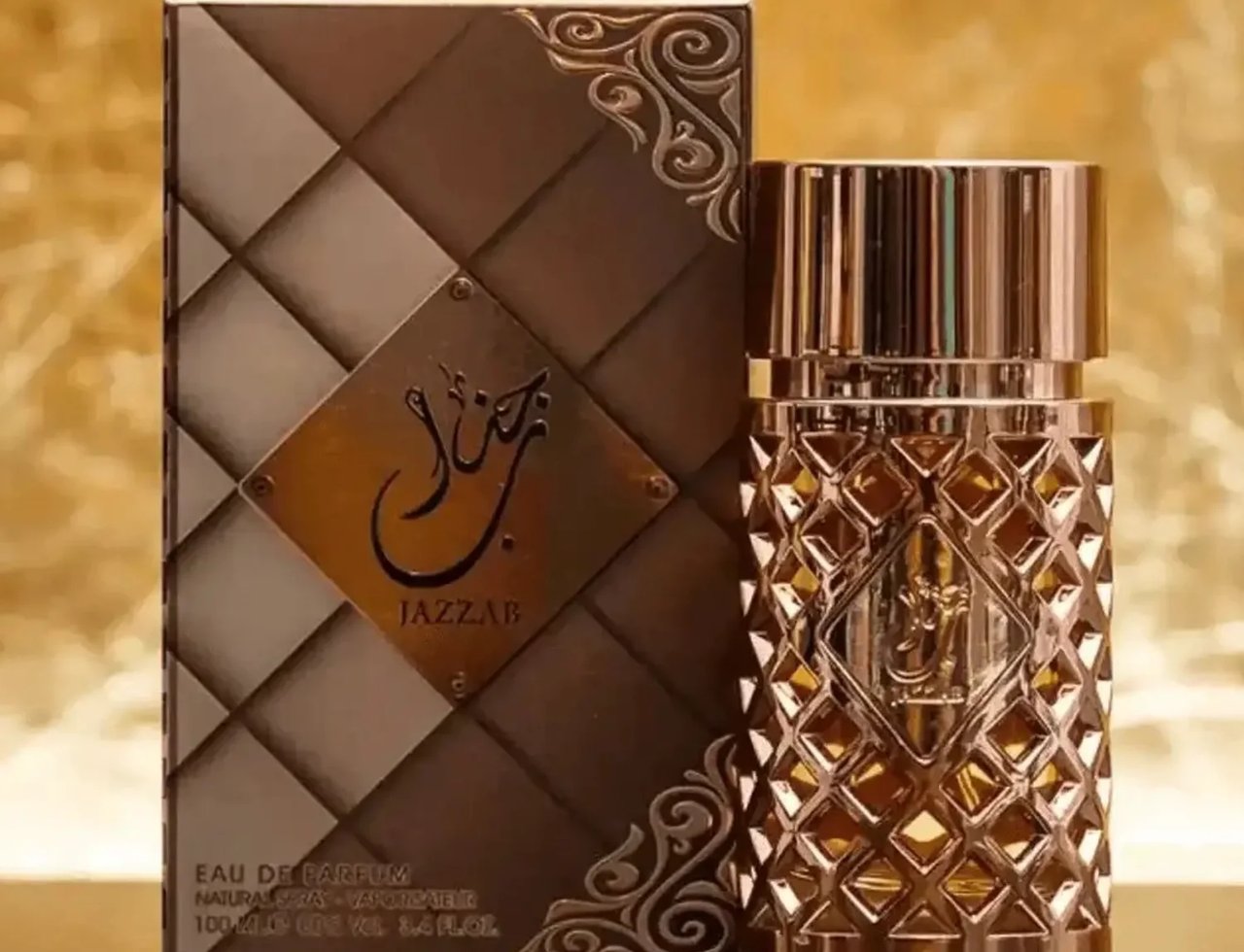 Ard Al Zaafaran Jazzab Gold Eau De Parfum 100ml — A gold-toned perfume bottle with a diamond-patterned glass body and a fluted cap, placed next to its matching textured brown and gold box on a reflective surface with a golden, textured background. | Ard Al Zaafaran Jazzab Gold Eau De Parfum 100ml — Botol minyak wangi