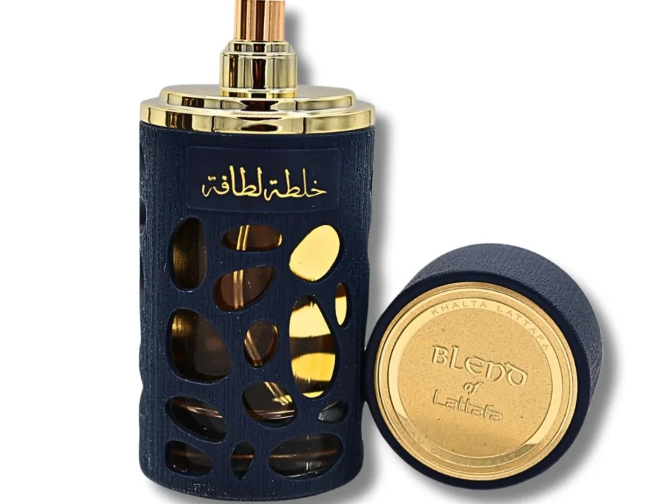 Lattafa Khalta Blend Of Lattafa Eau De Parfum 100ml — A dark blue textured perfume bottle with gold accents and cutouts revealing the amber liquid inside, next to its open gold-capped lid on a white background. | Lattafa Khalta Blend Of Lattafa Eau De Parfum 100ml — Botol minyak wangi biru gelap bertekstur dengan