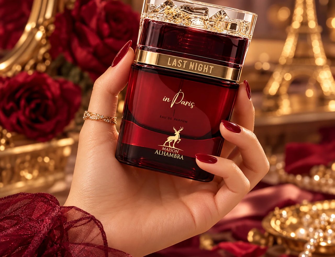 Maison Alhambra Last Night in Paris by Maison Alhambra 100ml Unisex — Tangan memegang botol minyak wangi kaca merah bertutup dan berlabel emas, dengan latar belakang bunga ros merah dan Menara Eiffel.
