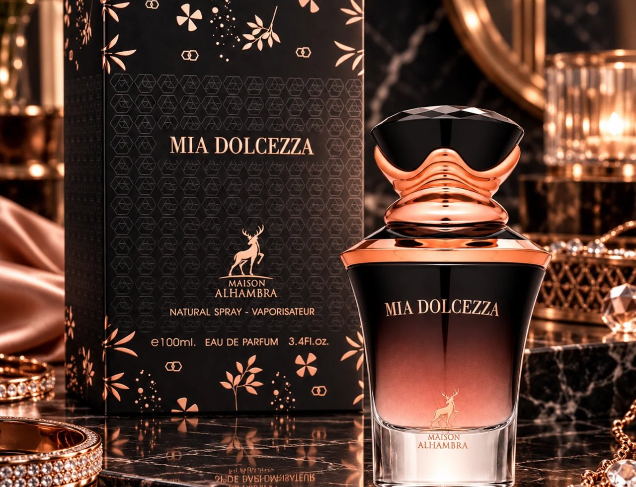 Maison Alhambra Mia Dolcezza — Kotak hitam dengan corak bunga emas ros dan logo rusa di sebelah botol minyak wangi hitam dan gradien emas ros dengan penutup hitam berfaset, di atas permukaan marmar bersama barang kemas.