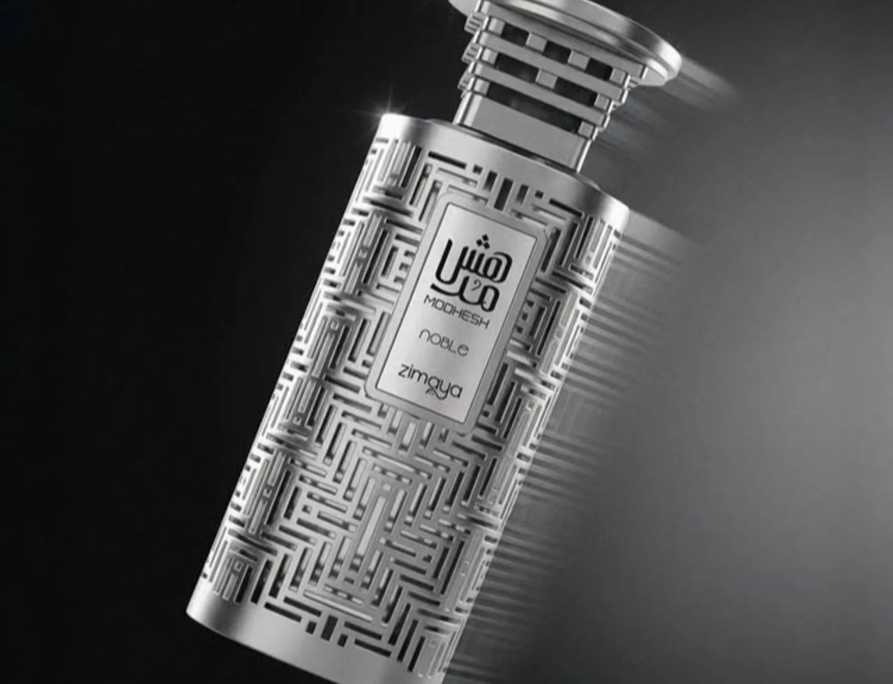 Zimaya Modhesh Noble 100ml by Zimaya — A silver, intricately patterned perfume bottle with a metallic cap, angled against a dark, gradient background with subtle lighting effects. | Zimaya Modhesh Noble 100ml by Zimaya — Botol minyak wangi berwarna perak dengan corak berukir rumit dan penutup logam, diletakkan condong