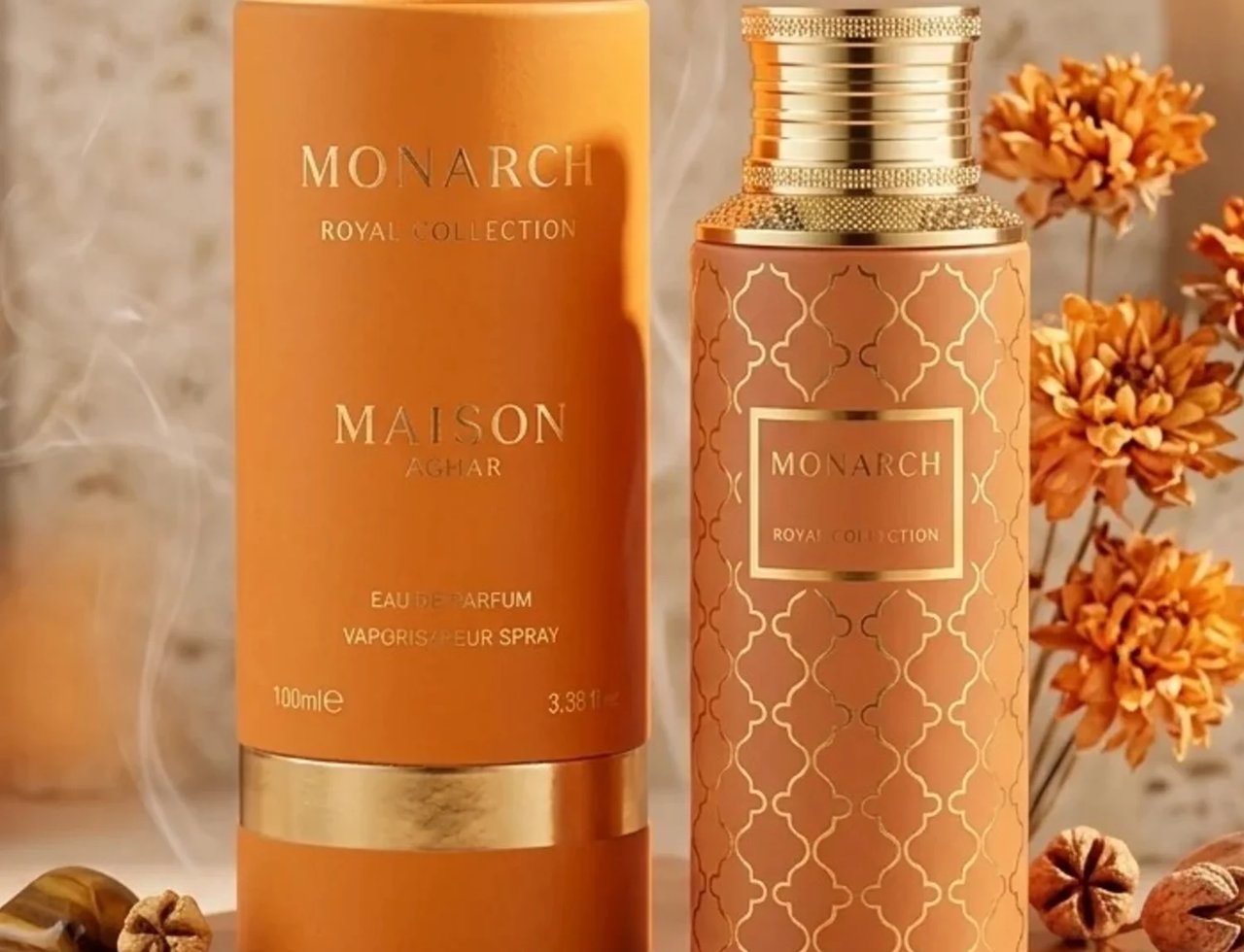 Maison Asrar Monarch by Maison Asrar 100ml EDP Unisex — Kotak silinder oren dan botol corak sepadan dengan aksen emas, dipamerkan bersama bunga kering dan batu mata harimau.