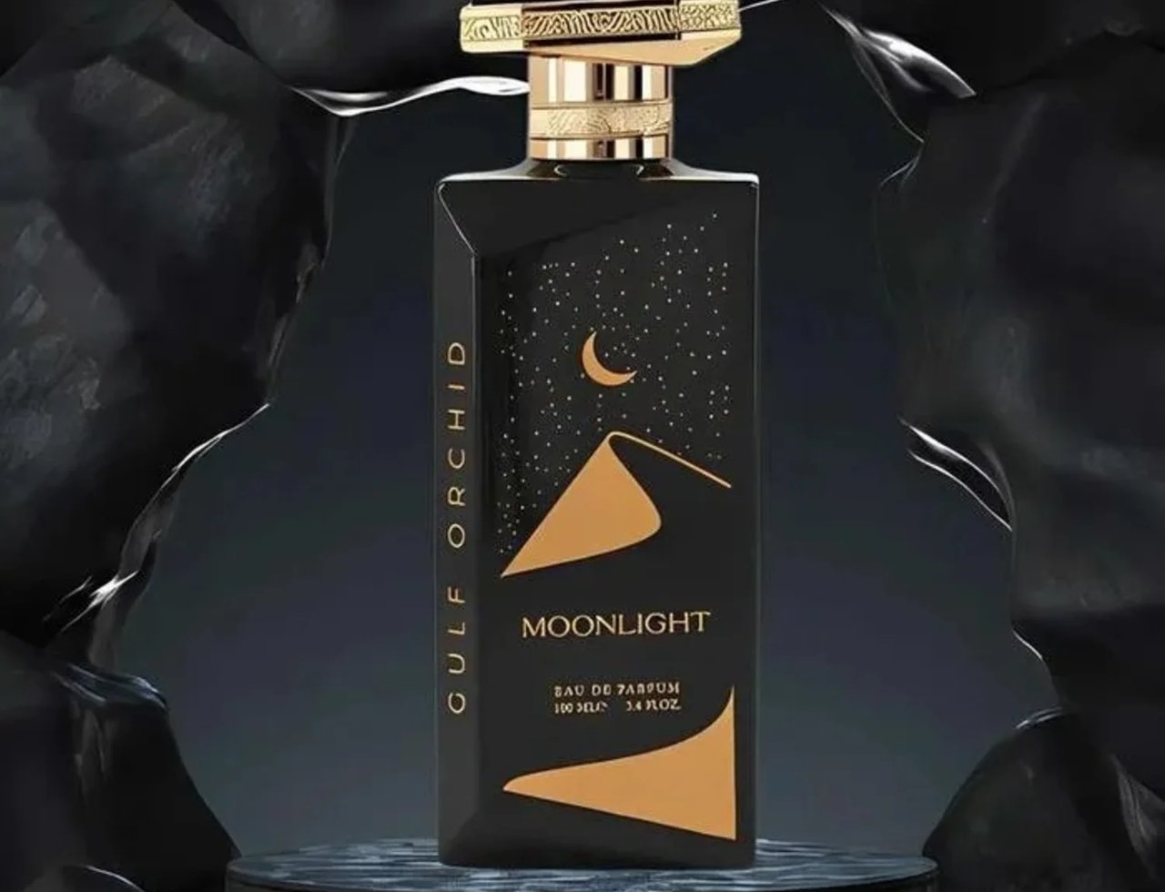 Gulf Orchid Moonlight Eau De Parfum 100ml by Gulf Orchid — A black perfume bottle with gold accents and a desert night scene on the label, displayed on a dark circular pedestal against a textured black background. | Gulf Orchid Moonlight Eau De Parfum 100ml by Gulf Orchid — Botol minyak wangi hitam dengan aksen emas
