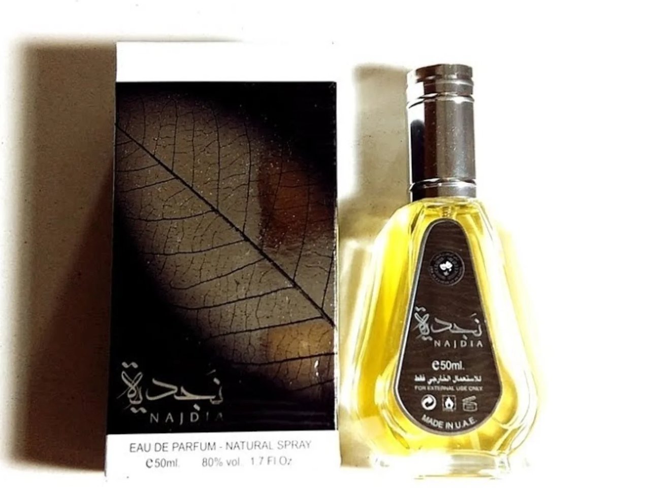 Ard Al Zaafaran Najdia 50ml EDP — A clear glass perfume bottle with yellow liquid and a silver cap, next to its dark box featuring a prominent leaf skeleton design.