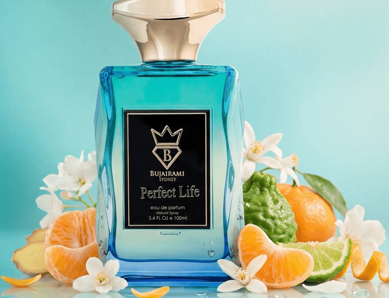 Bujairami Perfect Life by Bujairami Eau de Parfum 100ml — Botol minyak wangi kaca biru dengan penutup emas, dikelilingi buah sitrus, halia, dan bunga putih di latar belakang biru muda.