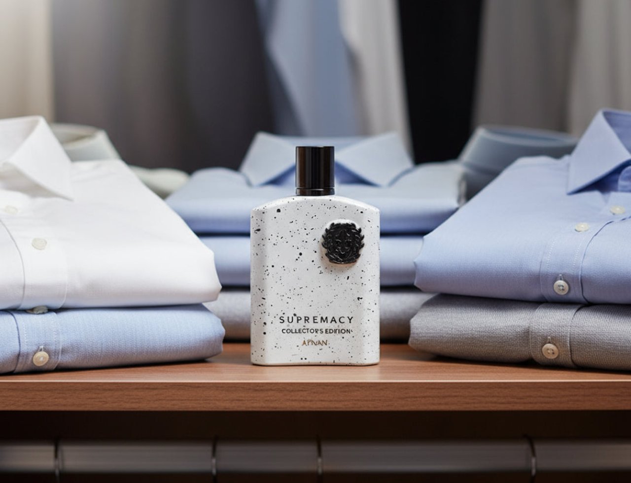 Afnan Supremacy Collector’s Edition by Afnan 100ml Men — Botol wangian putih bertitik hitam dengan penutup hitam, diletakkan di atas rak kayu berlatar belakang baju kemeja biru dan putih yang dilipat kemas.