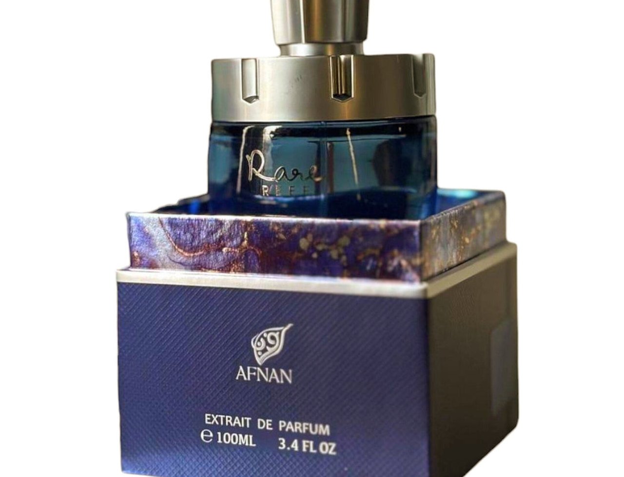 Afnan Rare Reef by Afnan 100ml Extrait de Parfum — Botol minyak wangi biru dengan penutup perak berkilat, diletakkan di atas kotak biru bertekstur dengan corak marmar ungu dan emas.