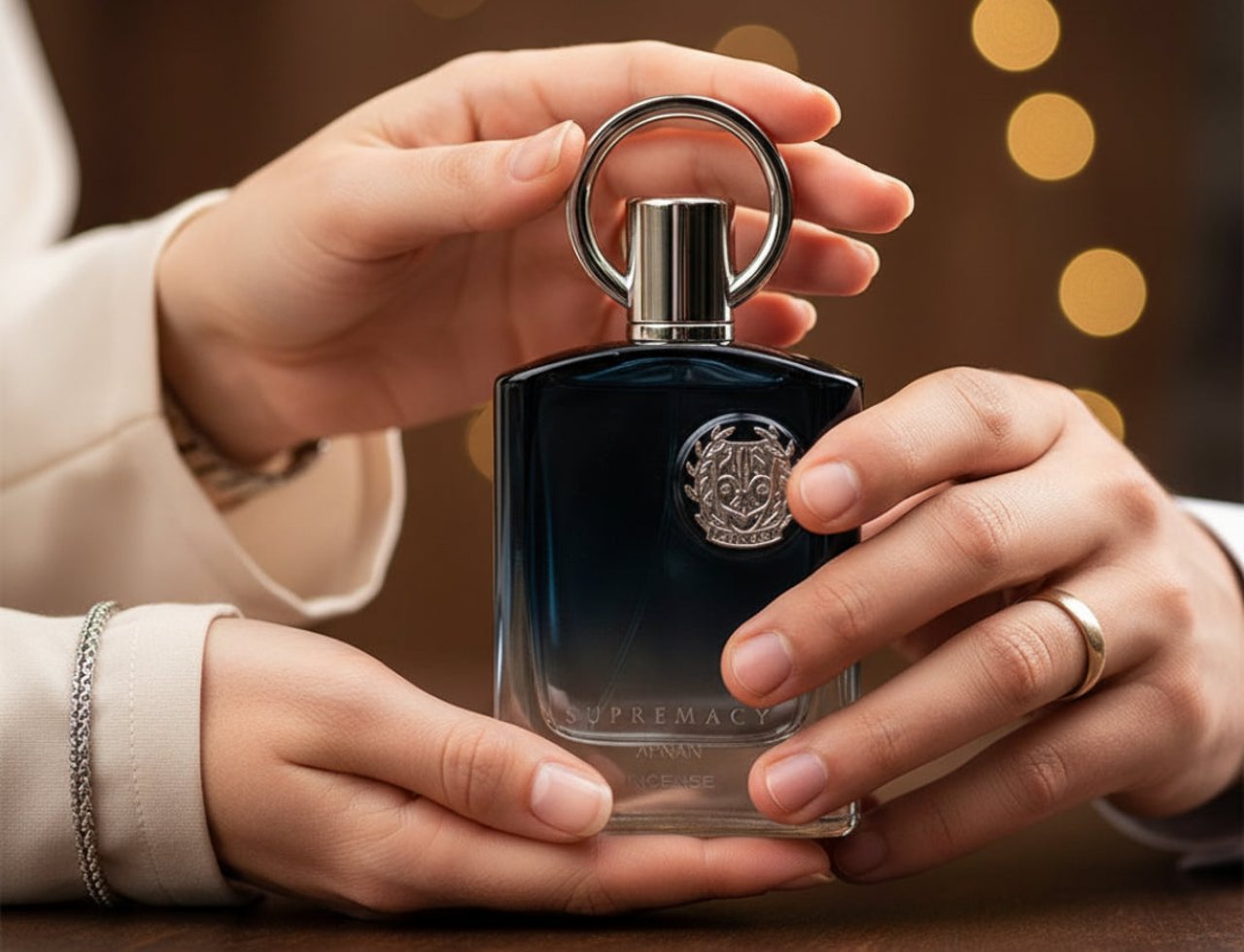 Afnan Supremacy Incense by Afnan Perfumes — Tangan memegang botol minyak wangi gelap dengan penutup logam berkilat dan cincin, latar belakang bokeh lembut.