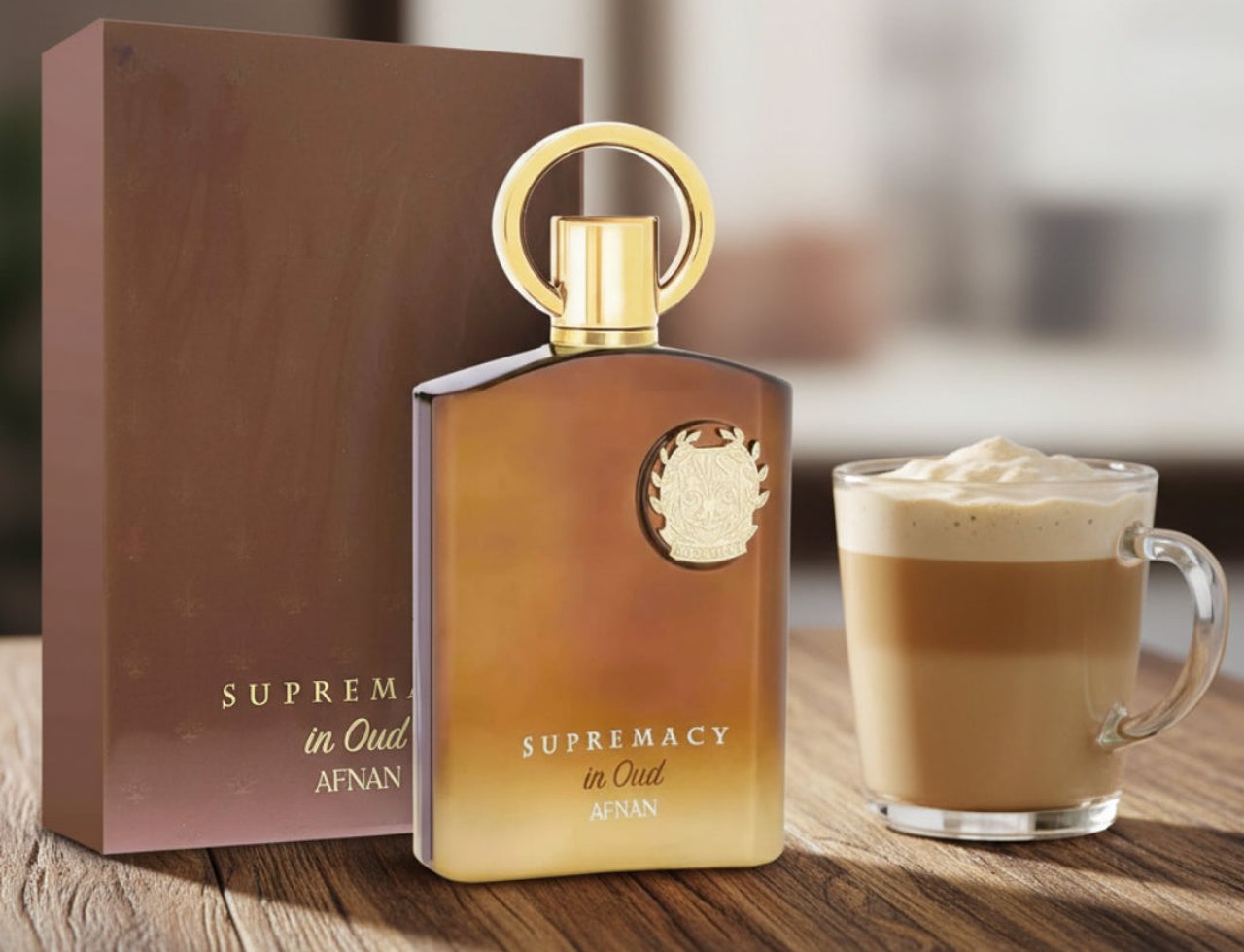Afnan Supremacy In Oud by Afnan Perfumes — Brown box and amber bottle next to a glass mug of layered coffee on a wooden table