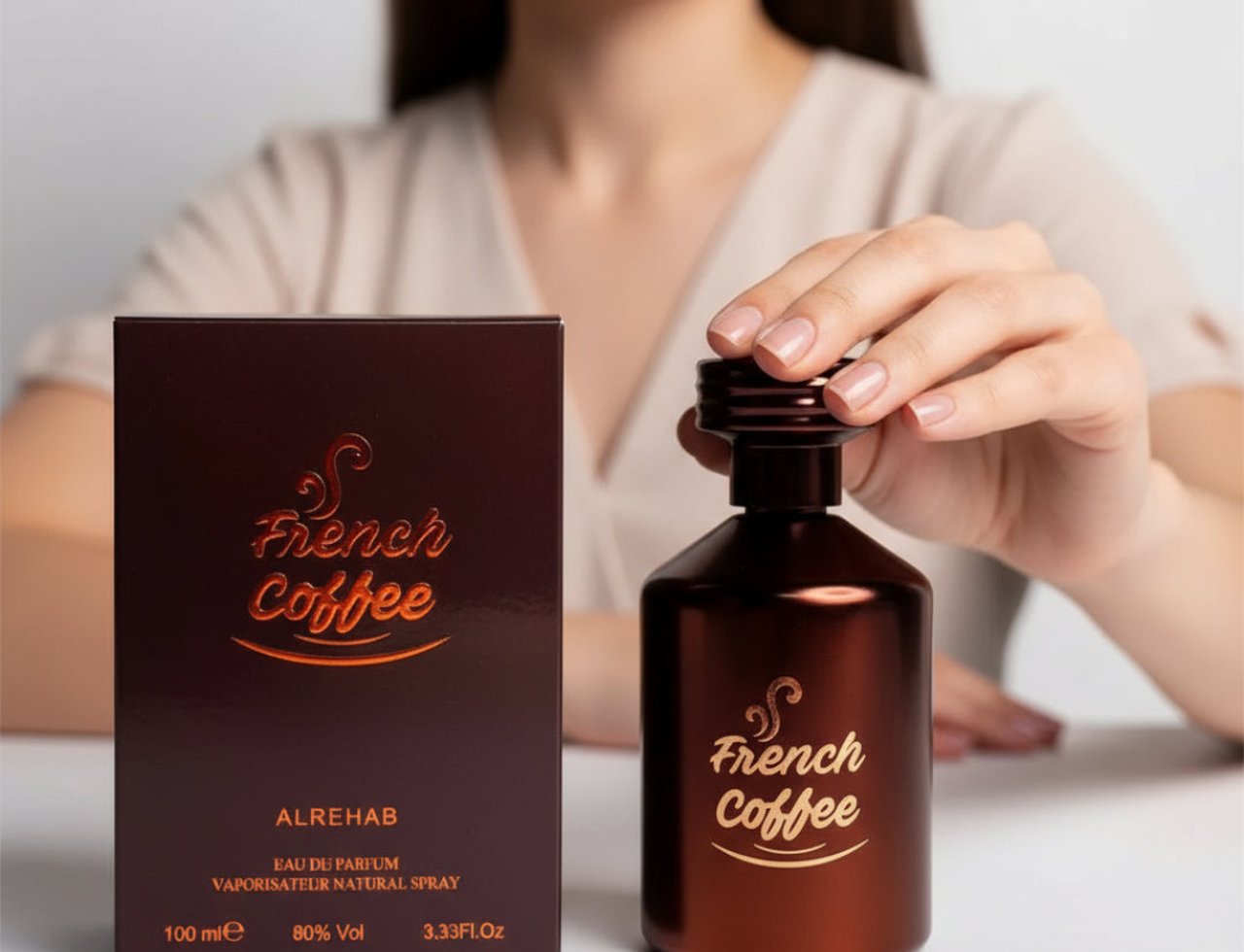 Al Rehab French Coffee — Tangan wanita memegang penutup botol minyak wangi coklat gelap berlogo "French Coffee" emas, bersebelahan kotak sepadan.