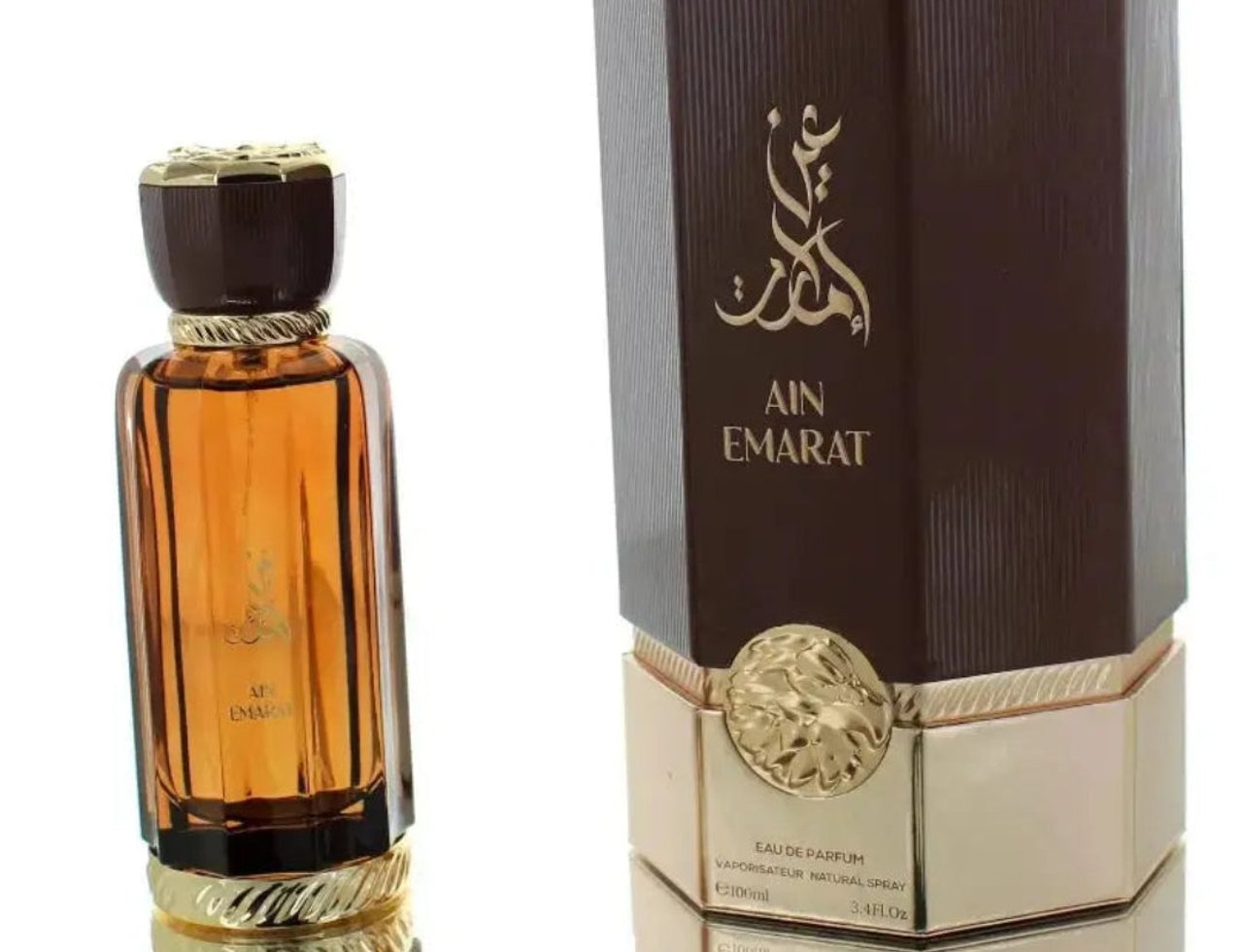 Al Wataniah Ain Emarat by Al Wataniah 100ml EDP – Intense Perfume, botol kaca perang dengan penutup emas berjalin, diletakkan di sebelah kotak coklat bertekstur dengan logo emas dan singa timbul