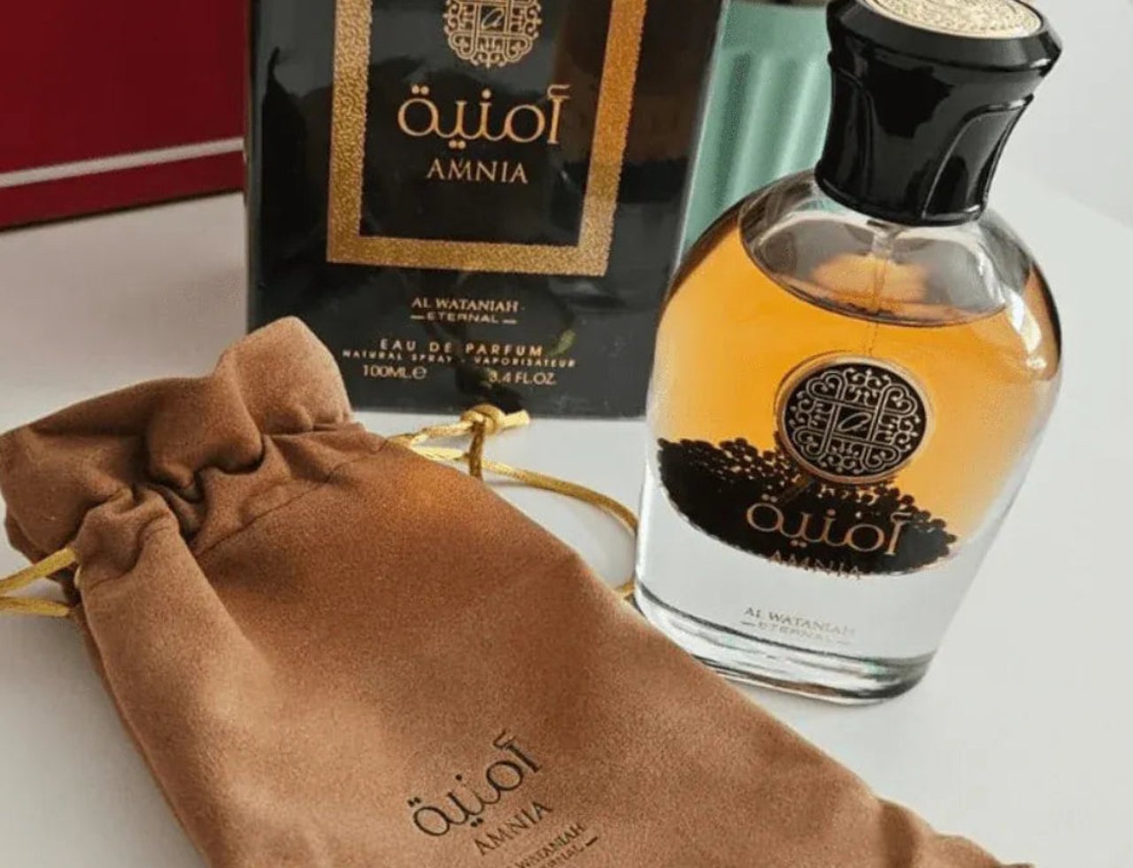 Al Wataniah Amnia by Al Wataniah For Her 100ml EDP — Perfume bottle and box with a brown drawstring pouch on a white surface.