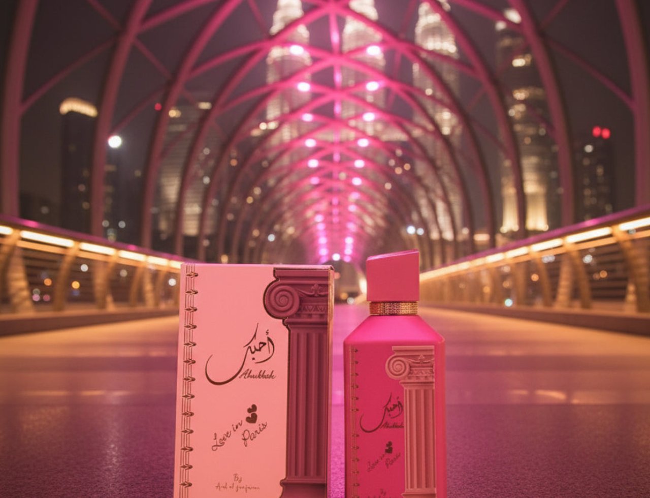 Ard Al Zaafaran Ahubbak Love In Paris EDP 100ml Zaafaran — Set wangian dalam kotak dan botol merah jambu, berlatarbelakangkan jambatan berlampu neon merah jambu terang dengan bangunan pencakar langit di kejauhan.