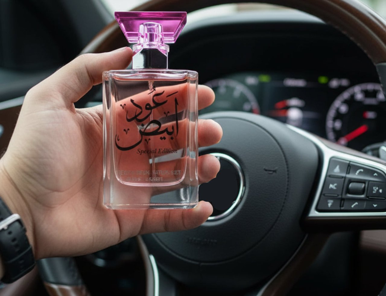 Ard Al Zaafaran Oud Abyad — Hand holding clear perfume bottle with pink cap inside a car