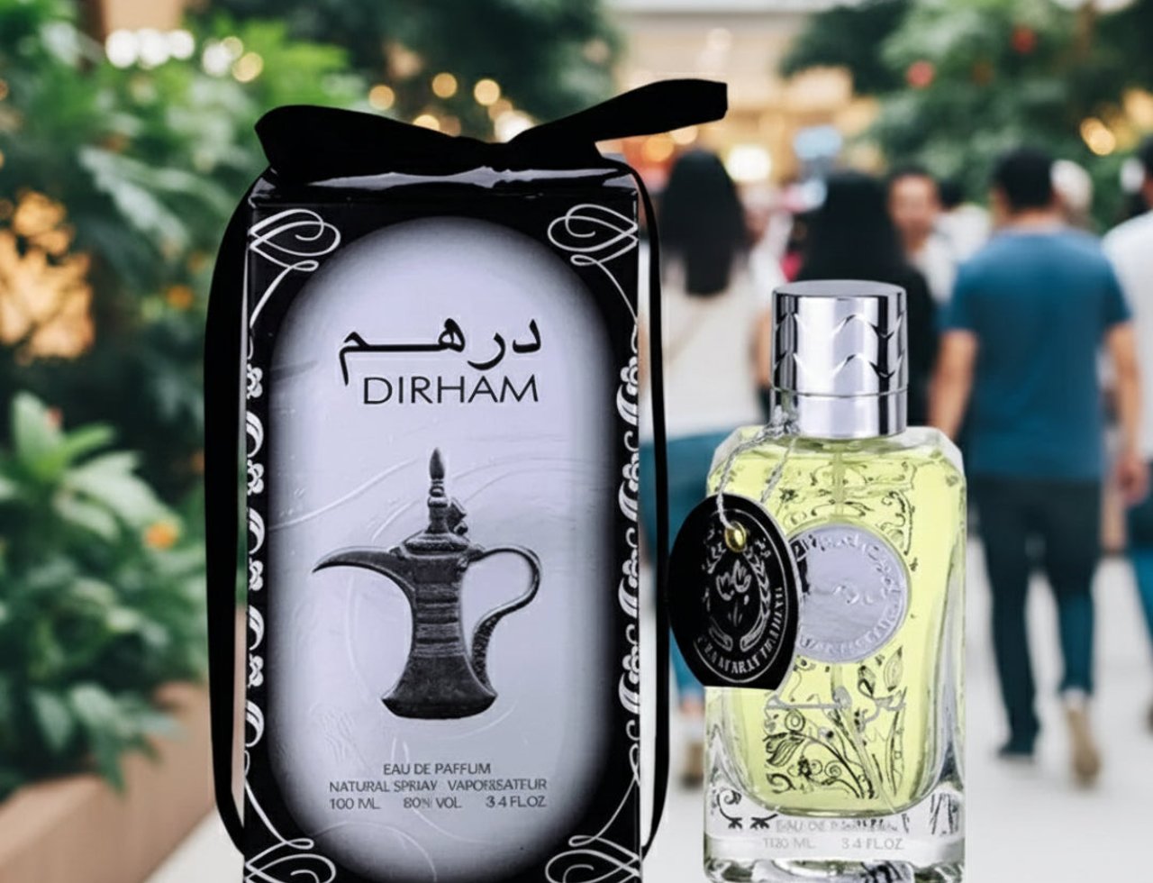 Ard Al Zaafaran Dirham By Ard Al Zaafaran Perfume For Him 100ml — Kotak wangian hitam dengan reben, botol kaca jernih berisi cecair kekuningan, dan latar belakang orang ramai di dalam bangunan
