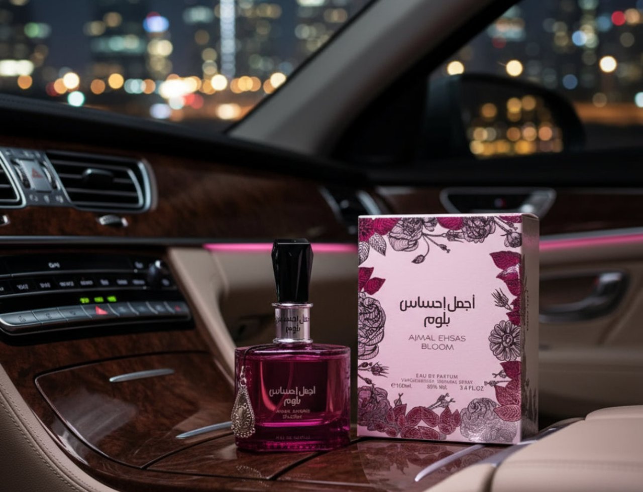 Ard Al Zaafaran Ajmal Ehsas Bloom — Pink perfume bottle and box on a car dashboard at night with city lights blurred in