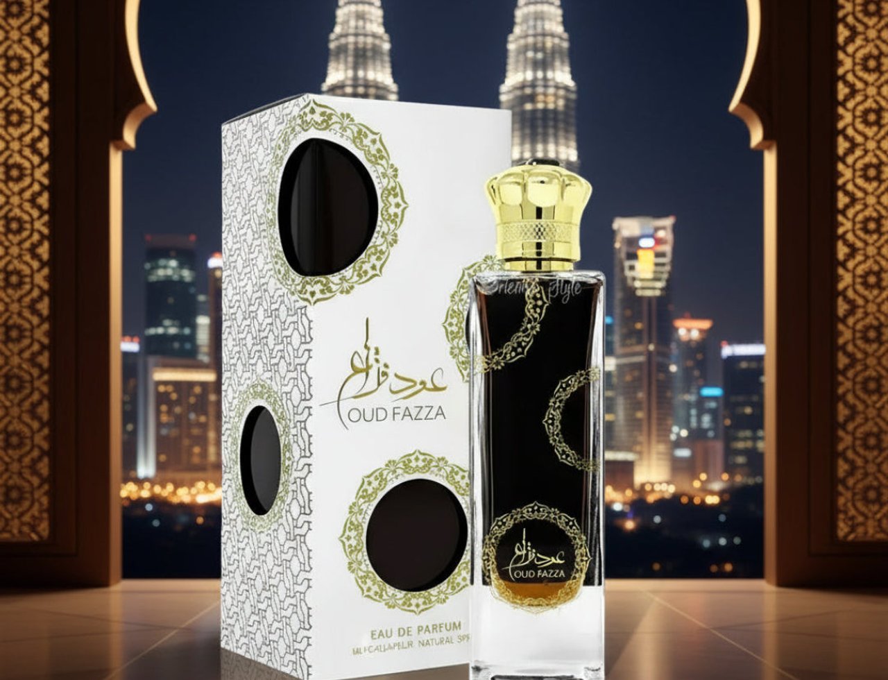 Ard Al Zaafaran Oud Fazza — Botol wangian kaca jernih dengan penutup emas, bersama kotak putih berhias corak emas, berlatar belakang bangunan pencakar langit waktu malam.