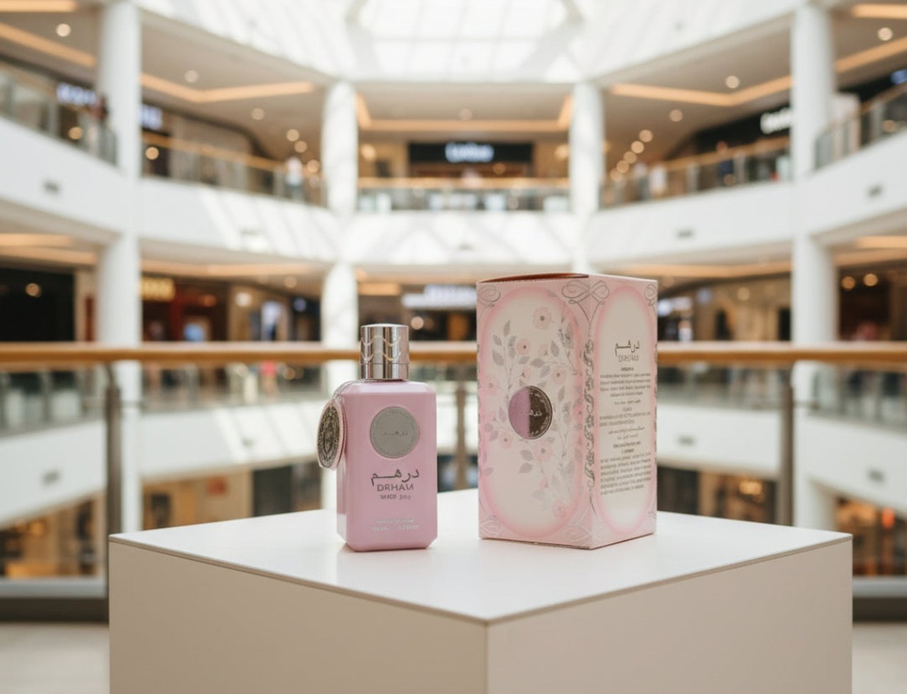 Ard Al Zaafaran Dirham Wardi by Ard Al Zaafaran 100ml EDP — Botol wangian merah jambu pastel dengan penutup perak dan tag, diletakkan di atas kubus putih di hadapan kotak wangian yang sepadan di dalam pusat membeli-belah yang terang