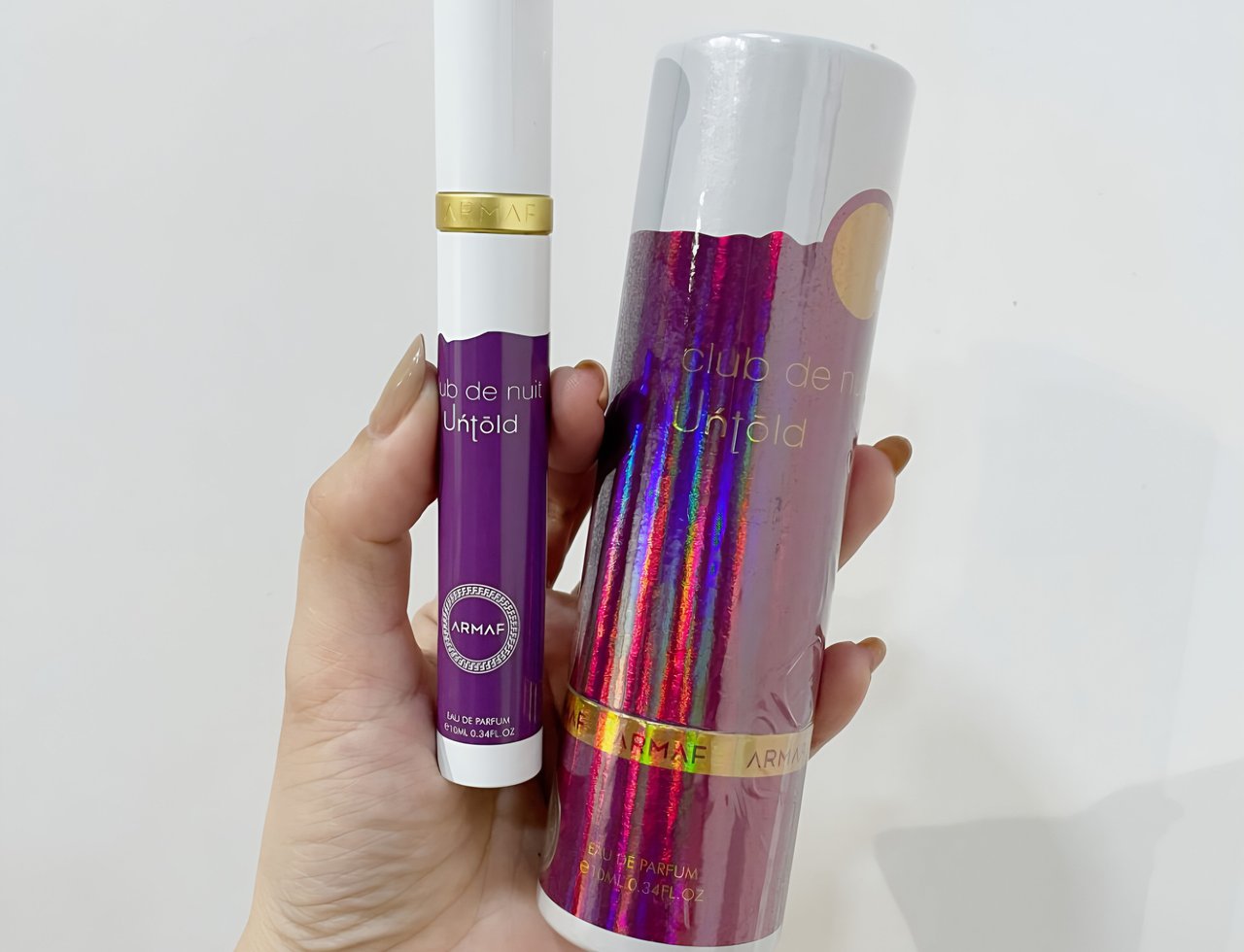 Armaf Club de Nuit Untold 10ml EDP – Unisex — Hand holding a purple travel spray and a matching cylindrical box with