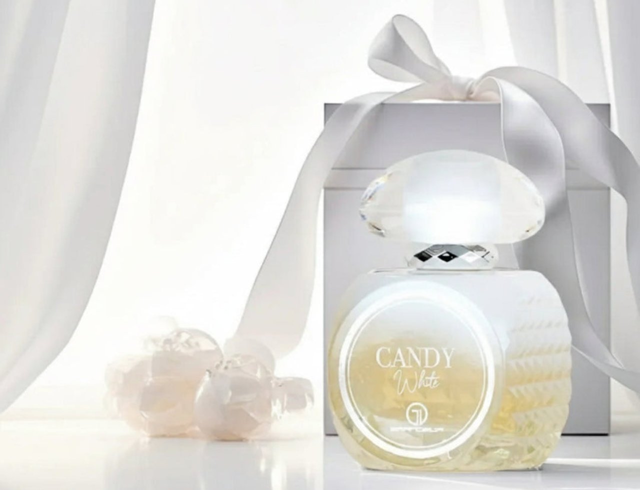 Grandeur Candy White by Grandeur – 100 ml for Women, a white perfume bottle with a faceted crystal-like cap, placed next to a white gift box tied with a satin ribbon, with sheer white curtains in the background.
