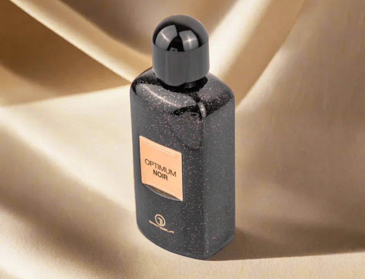Optimum Noir by Grandeur – Botol hitam berbintik dengan label emas, diletakkan di atas fabrik satin emas yang berlipat.