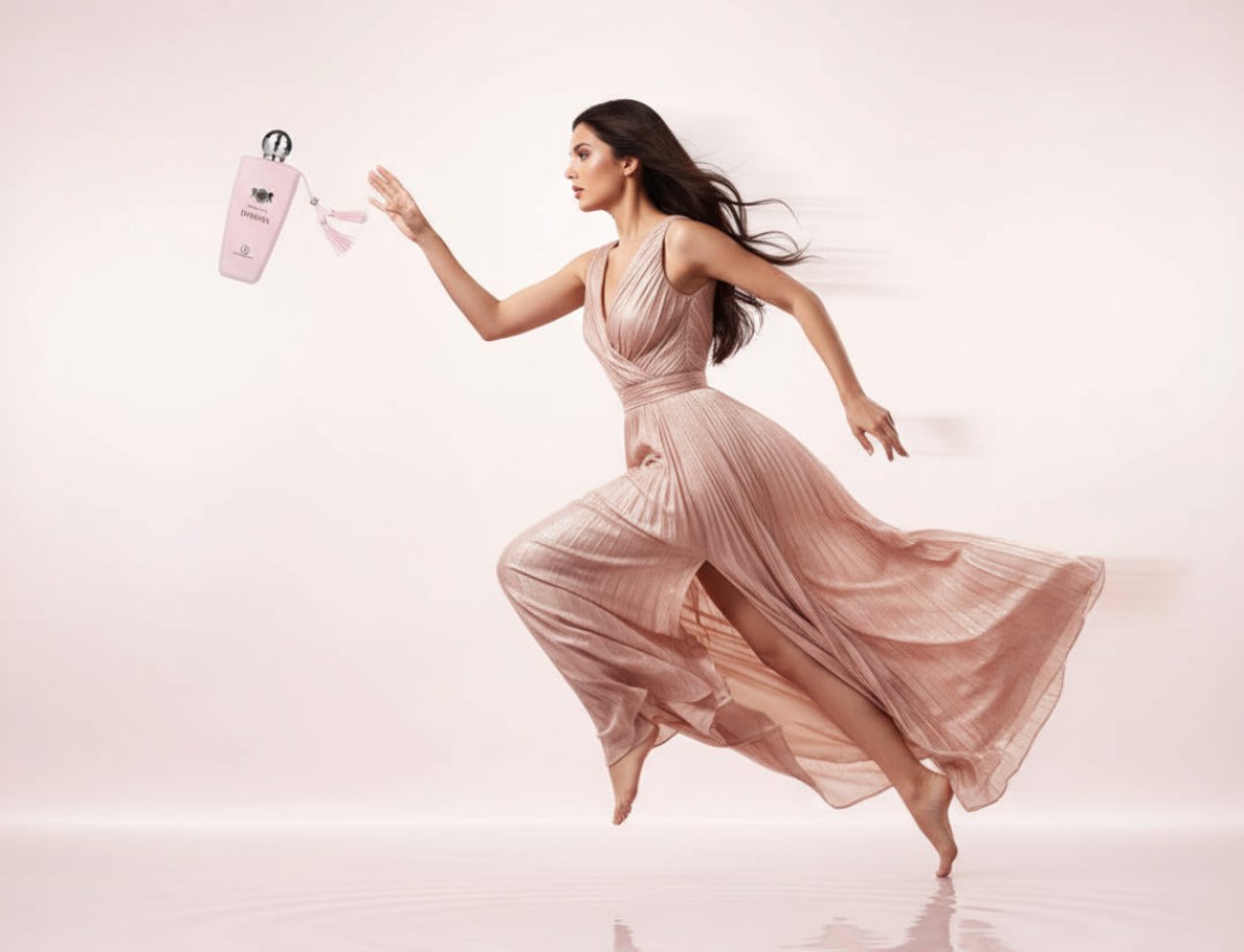 Grandeur Dakota by Grandeur Elite 100ml EDP – Women — Woman in a flowing pink dress leaping with a pink perfume bottle in hand against a soft pink background with water ripples below.