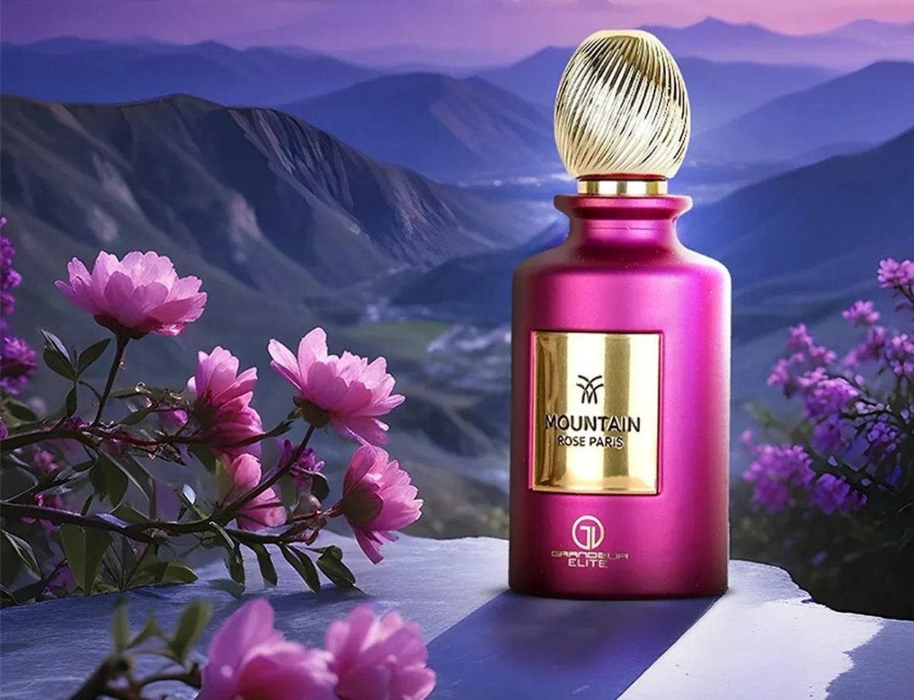 Grandeur Mountain Rose Paris 100ml EDP Grandeur Elite for Her — Botol minyak wangi merah jambu dengan penutup emas, berlatar belakang landskap pergunungan senja dengan bunga merah jambu di latar depan.