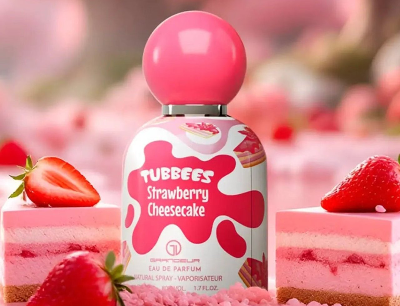 Grandeur Strawberry by Grandeur Tubbees 50ml Woman — Perfume bottle with pink spherical cap, surrounded by strawberry cheesecake slices and fresh strawberries, with a soft pink bokeh background.