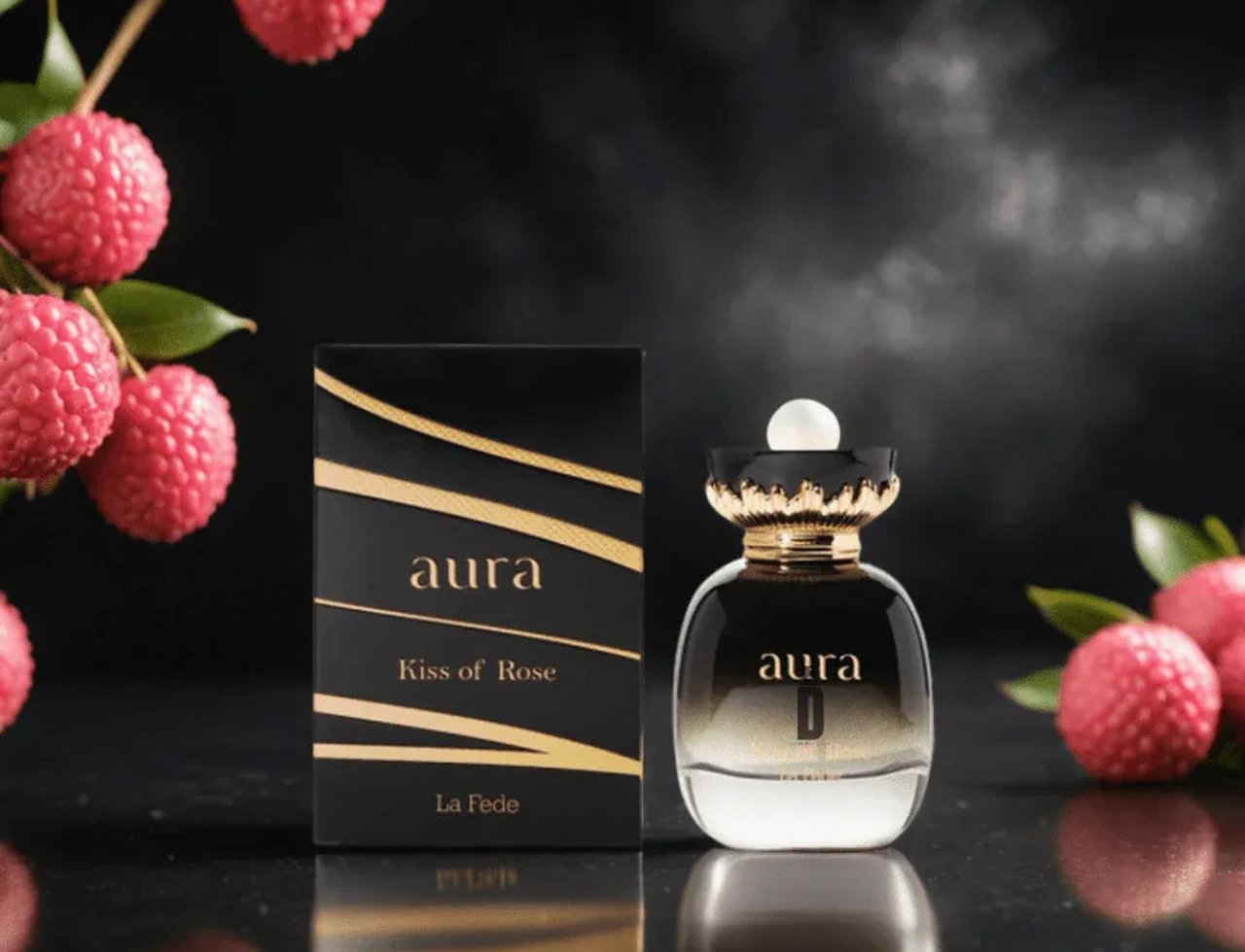 Khadlaj La Fede Elegant Kiss of Rose 100ml EDP — Black box with gold accents and a clear perfume bottle with a gold ornate cap, surrounded by lychee fruits on a dark reflective surface.