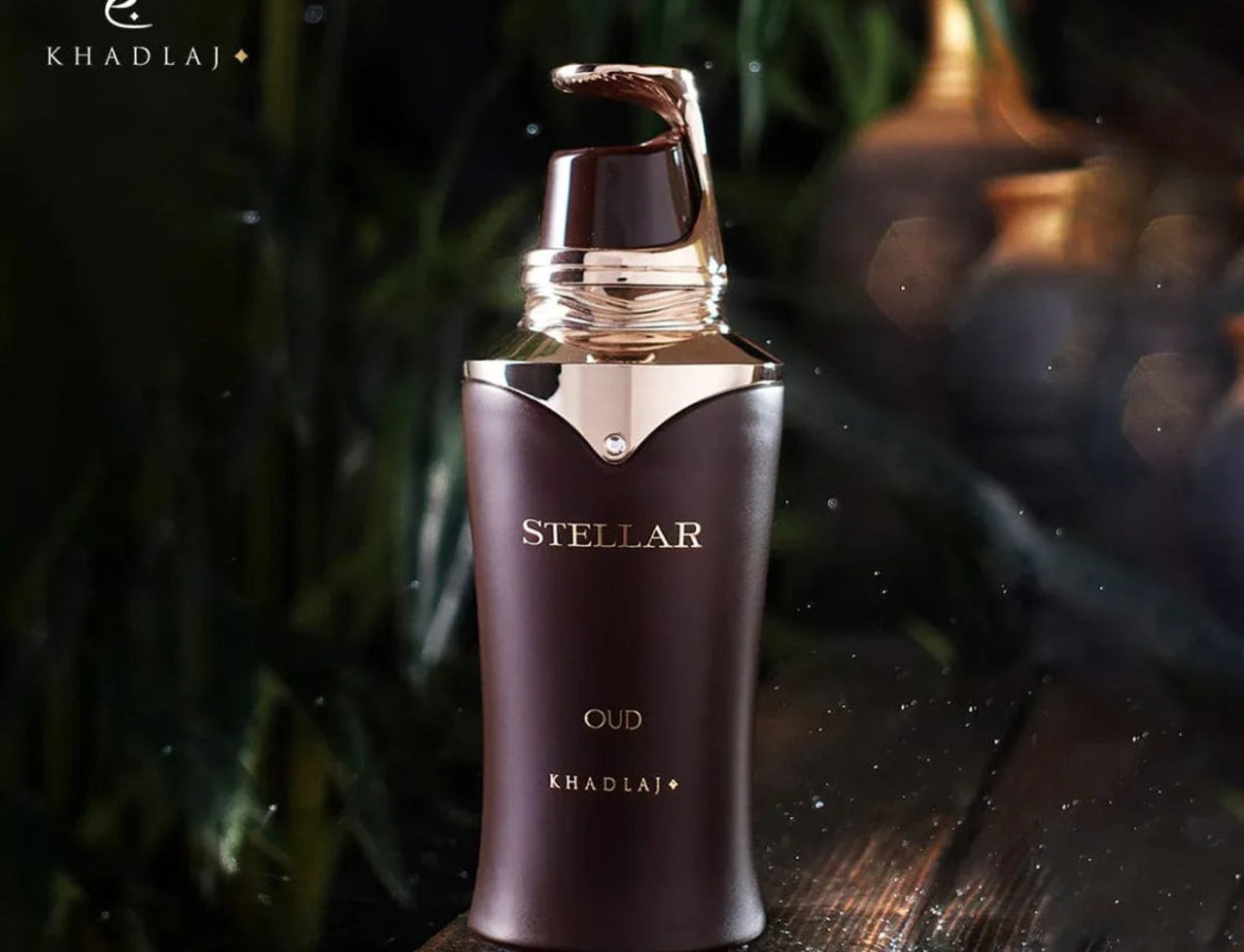 Khadlaj Stellar Oud by Khadlaj 100ml EDP Man — Botol minyak wangi coklat gelap dengan penutup dan aksen emas, tertulis 'STELLAR OUD KHADLAJ', berlatar belakang hijau dan emas kabur dengan titisan air di atas permukaan kayu.