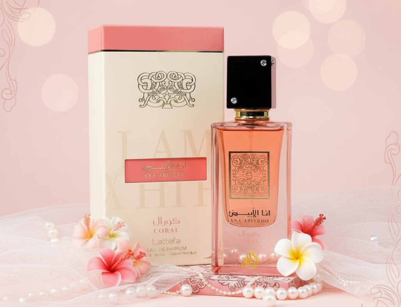 Lattafa Ana Abiyedh Coral — Botol wangian berwarna jingga dengan kotak sepadan, dihiasi bunga-bunga kecil dan mutiara di atas kain merah jambu lembut.