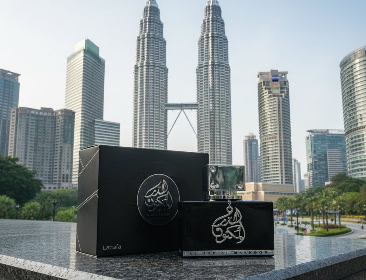 Lattafa Al Dur Al Maknoon Silver 100ml EDP Men — Kotak dan botol wangian hitam berkilau dengan logo perak, berlatar belakang bangunan pencakar langit berkembar yang ikonik.