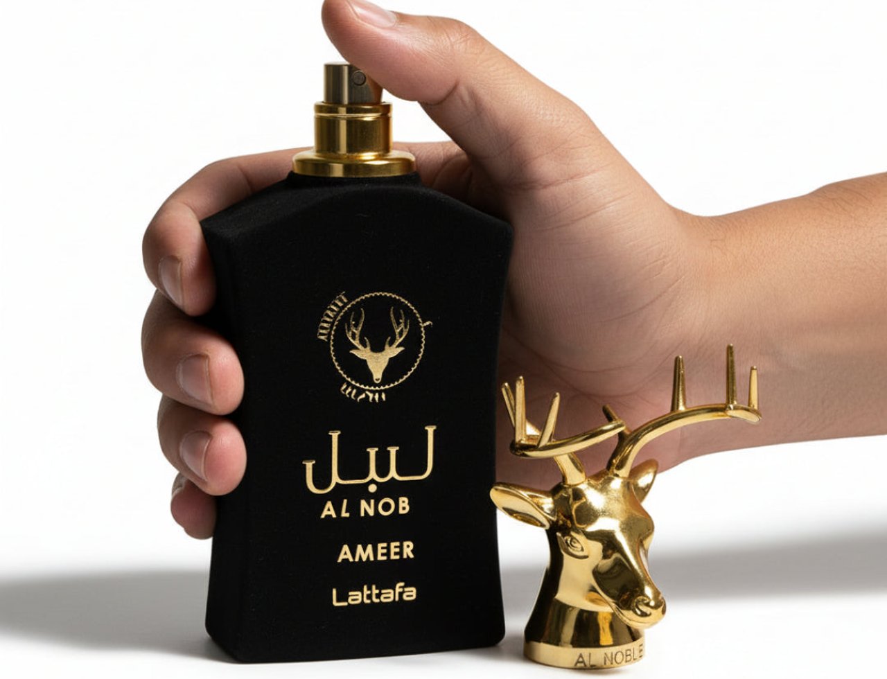 Lattafa Al Noble Ameer by Lattafa 100ml EDP Men — Tangan memegang botol minyak wangi hitam baldu dengan penutup emas, di sebelah patung kepala rusa emas kecil di atas tapak berlabel 'AL NOBLE'