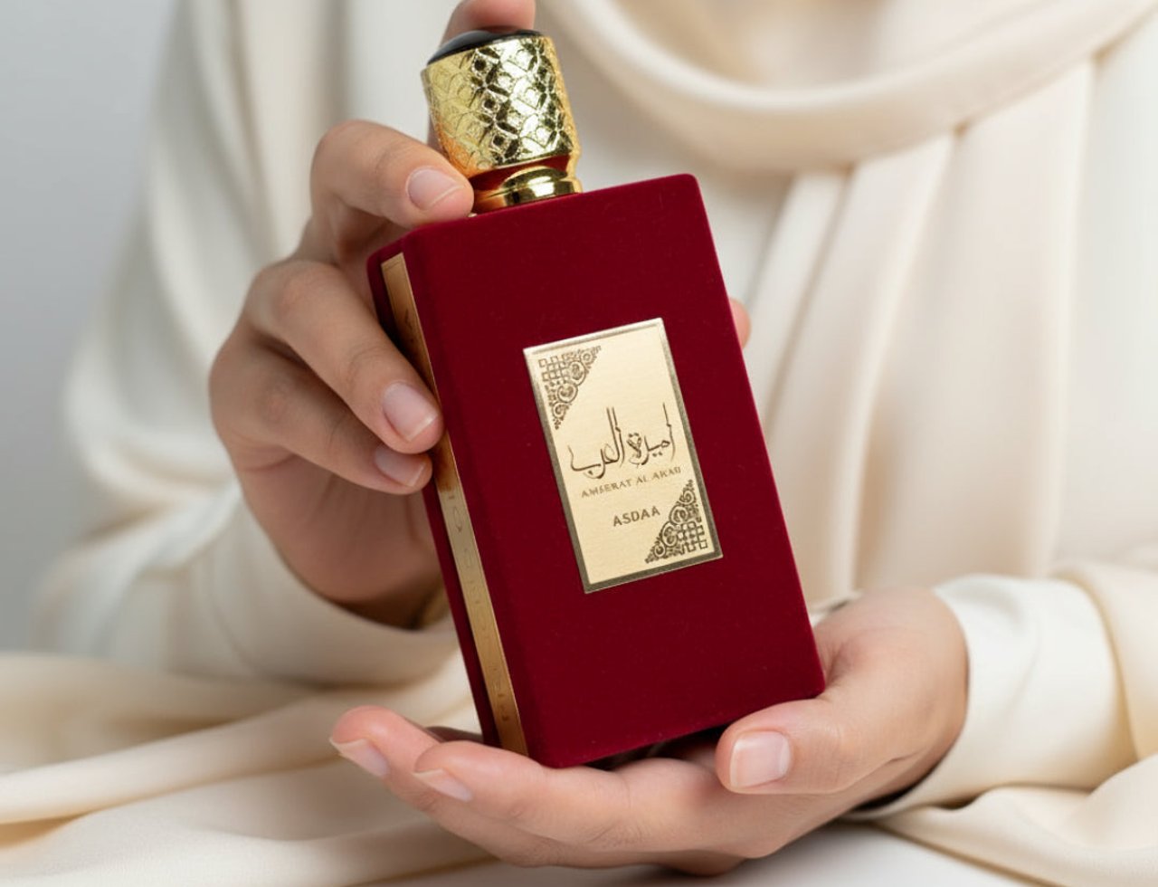 Asdaaf Ameerat Al Arab by Lattafa Women 100ml — Tangan memegang botol minyak wangi merah baldu dengan penutup emas berukir dan label emas bertulis tulisan Arab dan 'ASDOAA'