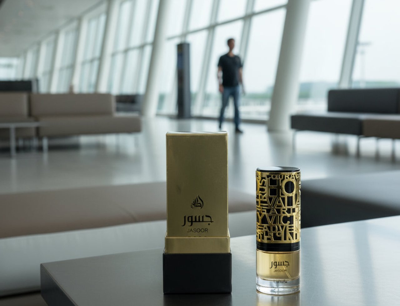 Lattafa Jasoor by Lattafa Perfumes 100 ml Unisex — Gold perfume box and bottle with Arabic calligraphy on a dark table in a modern airport lounge.