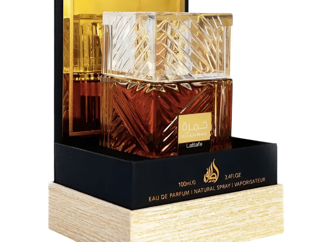 Lattafa Khamrah by Lattafa 100ml EDP Unisex — Botol minyak wangi kaca perang amber dengan penutup jernih berfaset, dipamerkan dalam kotak hitam dan emas dengan tapak bertekstur kayu.