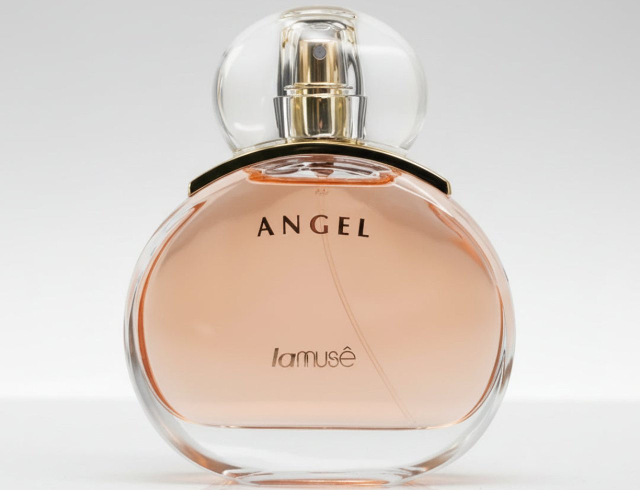 Lattafa Angel by LaMuse — Botol kaca bulat berisi cecair berwarna merah jambu lembut, dengan penutup bulat lutsinar dan perincian emas di leher botol. Teks 'ANGEL' dan 'lamusê' tertulis di hadapan botol.