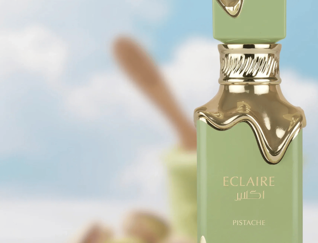 Lattafa Eclaire Pistache by Lattafa 100ml EDP Unisex — Botol minyak wangi hijau pastel dengan penutup dan hiasan emas berkilat, latar belakang langit biru dan awan, dengan kacang pistachio dan alat di latar belakang kabur.