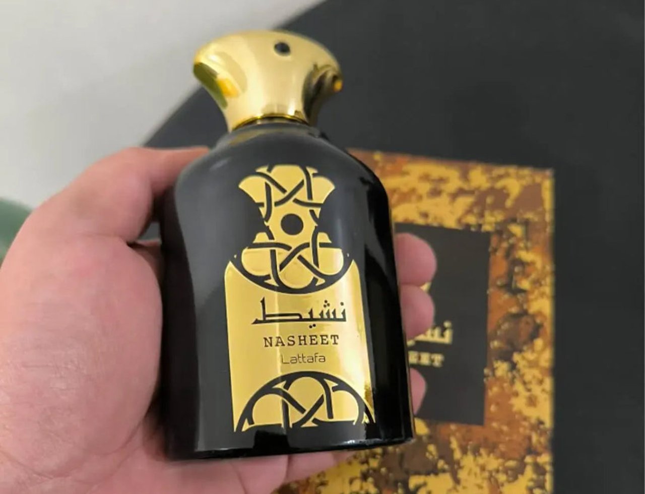 Lattafa Nasheet by Lattafa Perfume 100ml EDP Unisex — Black perfume bottle with gold cap and gold label held in a hand, with the product box blurred in the background.