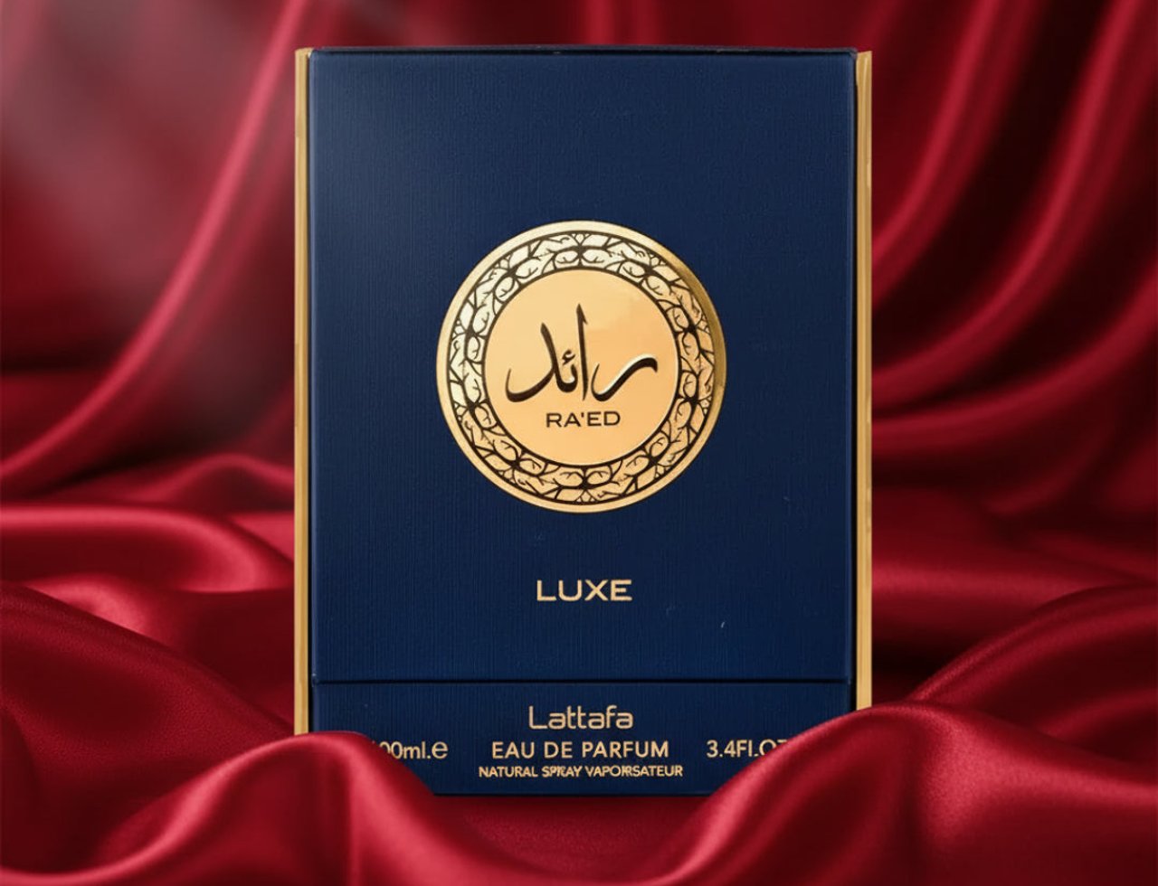 Lattafa Raed Luxe by Lattafa 100ml EDP Unisex — A navy blue perfume box with a gold circular emblem featuring Arabic script and 'RA'ED' text, set against a luxurious draped red satin background.