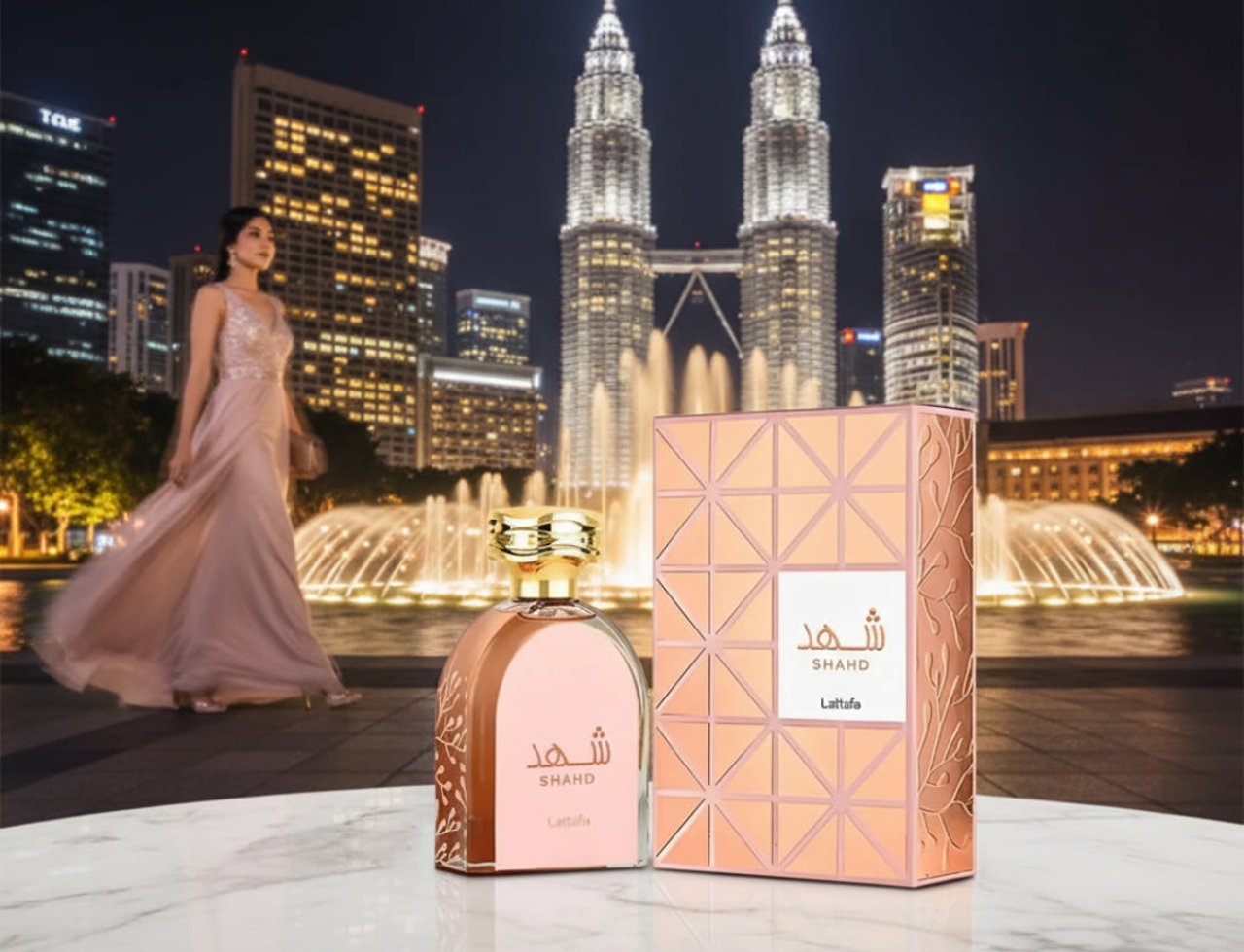 Lattafa Shahd oleh Lattafa Perfumes 100 ml Wanita — Seorang wanita berbaju membelakangi botol dan kotak minyak wangi, dengan latar belakang Menara Berkembar Petronas dan pancutan air pada waktu malam.