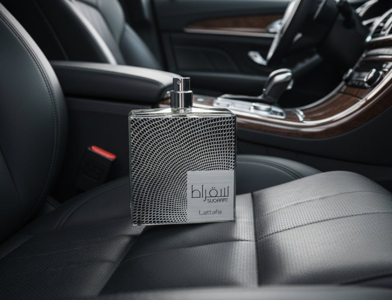 Lattafa Suqraat by Lattafa 100ml EDP Men — Botol minyak wangi kaca berbentuk segi empat dengan corak perak bertekstur diletakkan di atas tempat duduk kereta kulit hitam, dengan bahagian dalam kereta kelihatan di latar belakang.