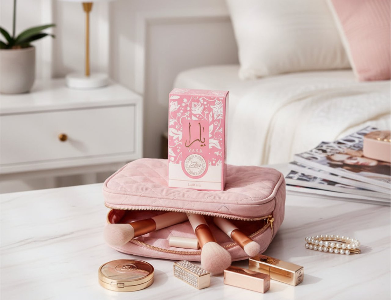 Lattafa Yara Elixir by Lattafa 100ml EDP — Pink quilted makeup bag with makeup brushes, a pink floral patterned box, compact powder, lipstick, and pearl bracelet on a marble surface.