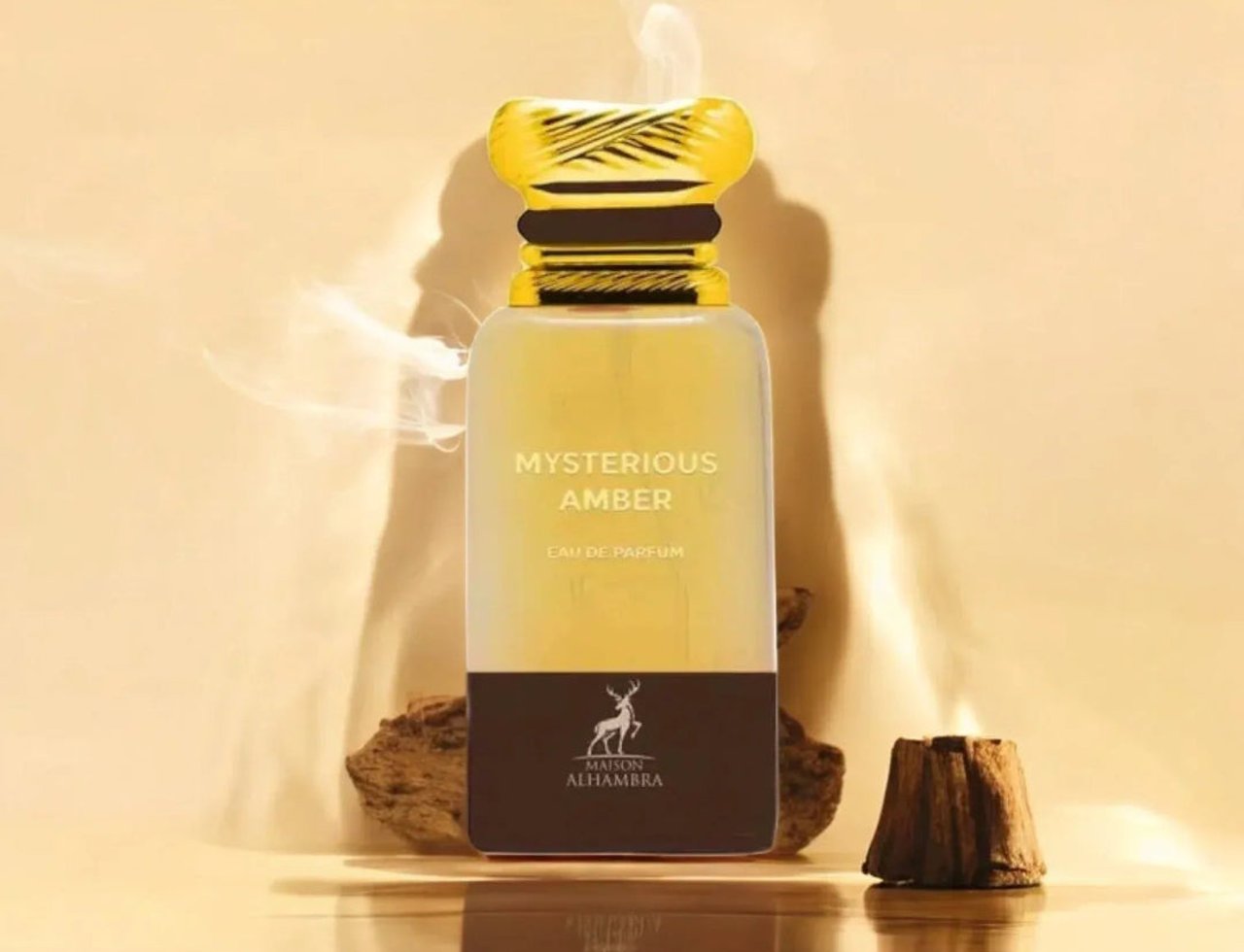 Maison Alhambra Mysterious Amber 80ml — Botol minyak wangi kaca jernih dengan penutup emas, tertulis 'MYSTERIOUS AMBER EAU DE PARFUM' dan logo Maison Alhambra, dikelilingi serpihan kayu dan kesan asap berlatar belakang emas.