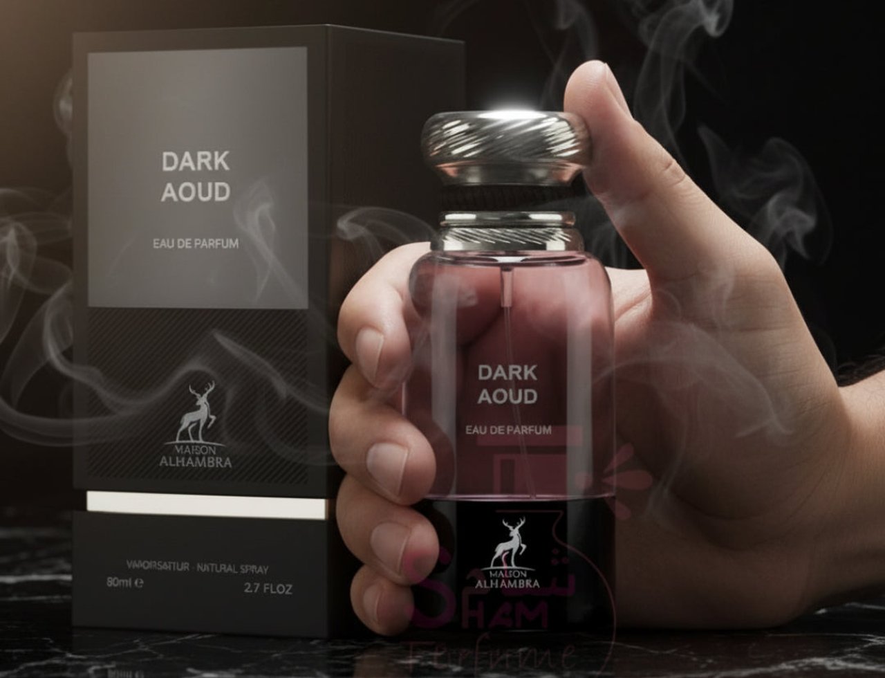 Maison Alhambra Dark Aoud — Hand holding a glass perfume bottle with a silver cap, next to its dark box, with wisps of smoke.