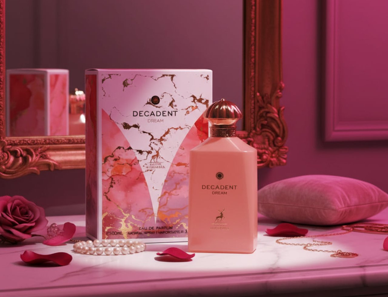 Maison Alhambra Decadent Dream — Botol dan kotak wangian merah jambu dengan aksen marmar dan emas, kelopak mawar, gelang mutiara, dan rantai emas di atas permukaan marmar.