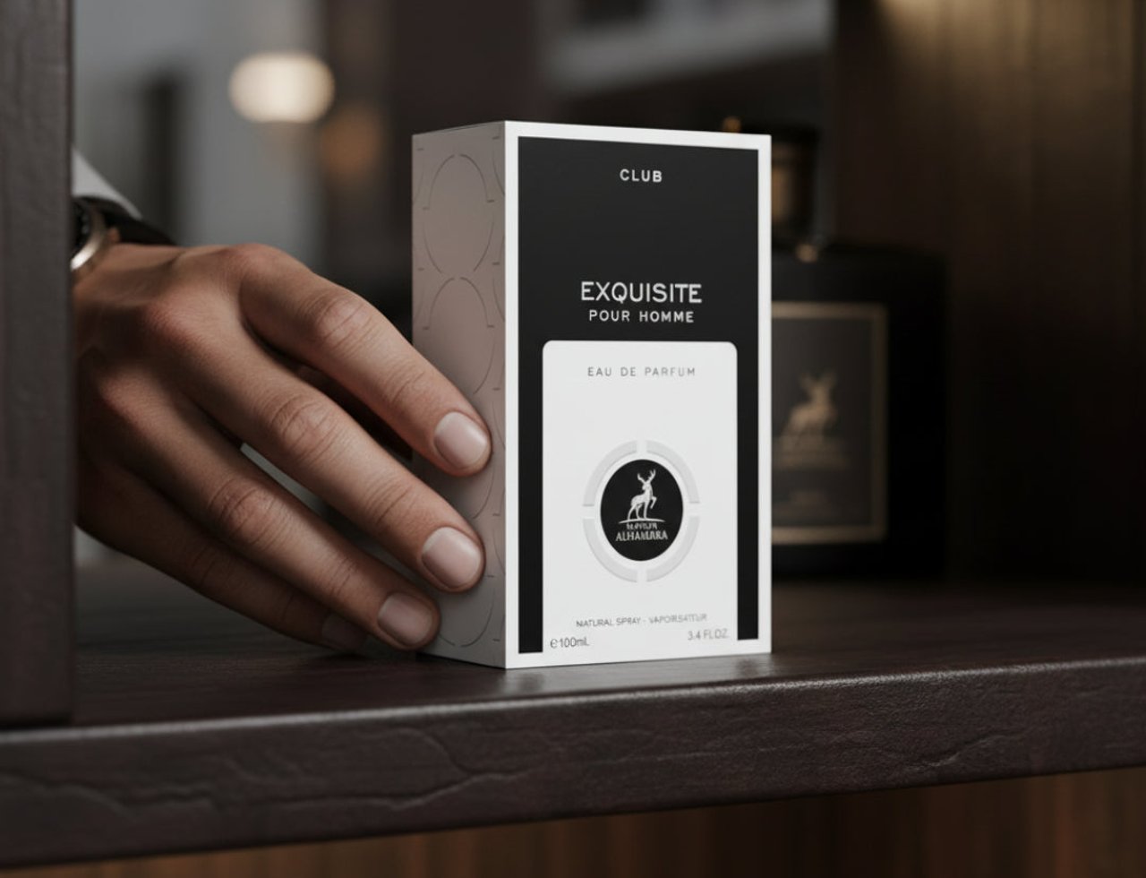 Maison Alhambra Exquisite Club By Maison Alhambra For Men 100ml — Tangan mencapai kotak minyak wangi di rak, dengan botol gelap di latar belakang.